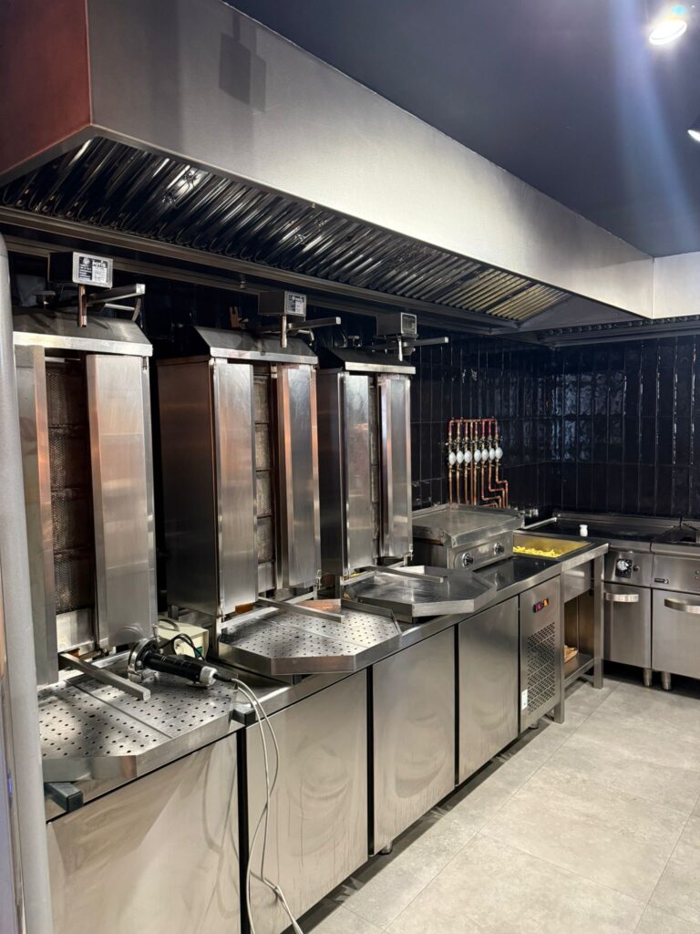 Línea De Asadores De Kebab Verticales Y Campana Extractora Industrial En Cocina Profesional